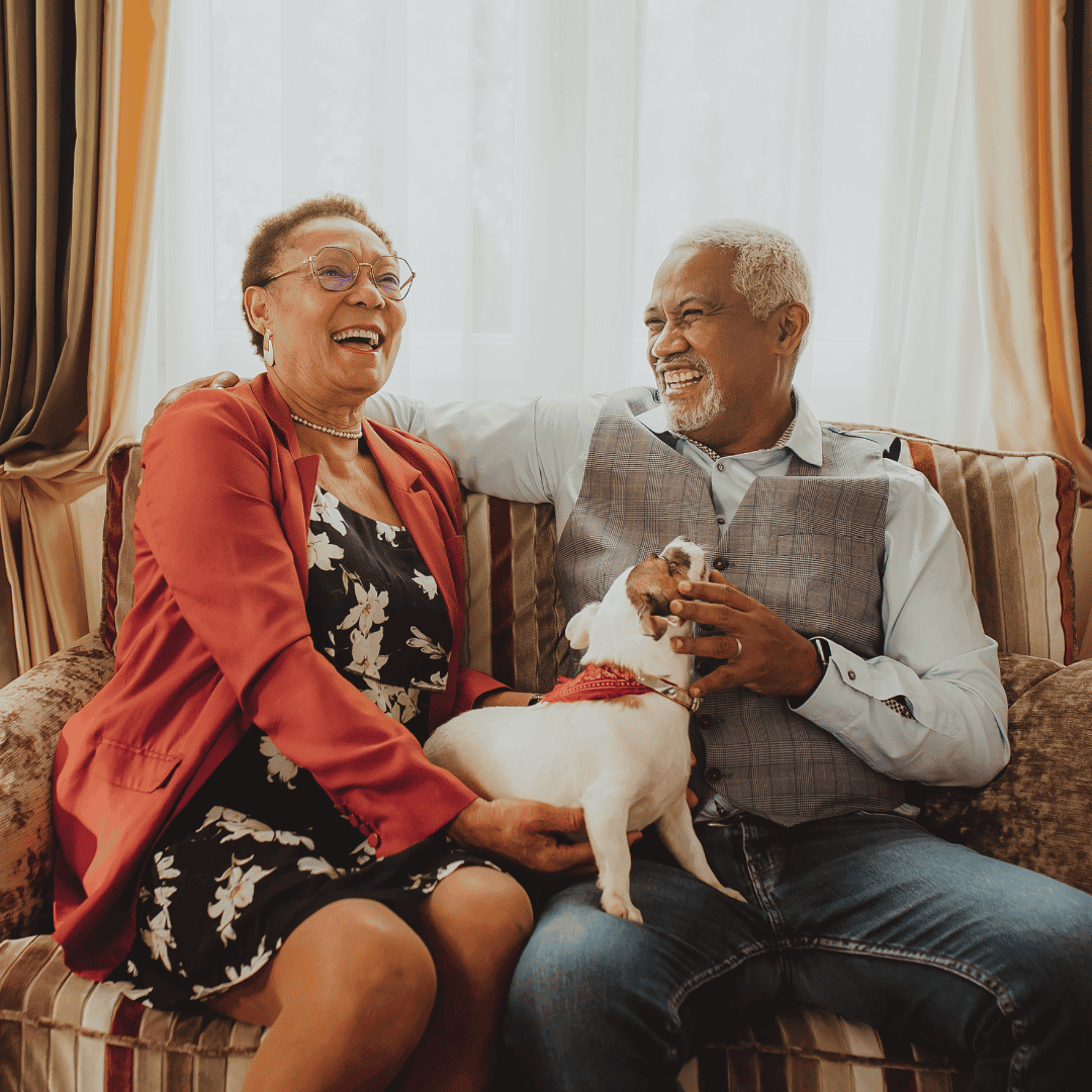 Pareja mayor feliz con un perro pequeño en el sofá de la sala.