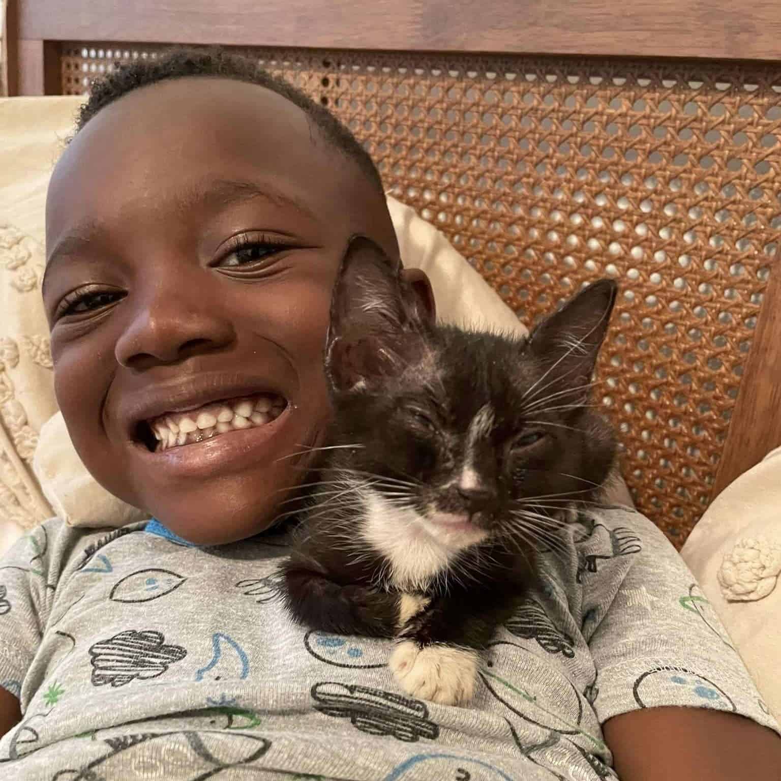 Happy boy cuddling with a black and white cat, both looking content and relaxed.