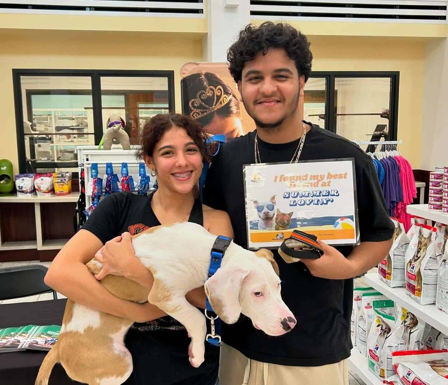 Dos voluntarios sonriendo con un perro en un evento de adopción de mascotas de Peggy Adams.