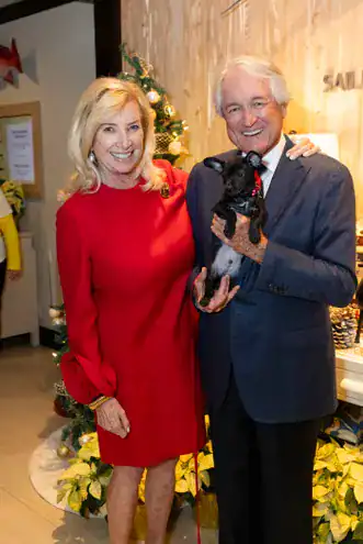 A woman and man smiling with a small dog at a festive event.