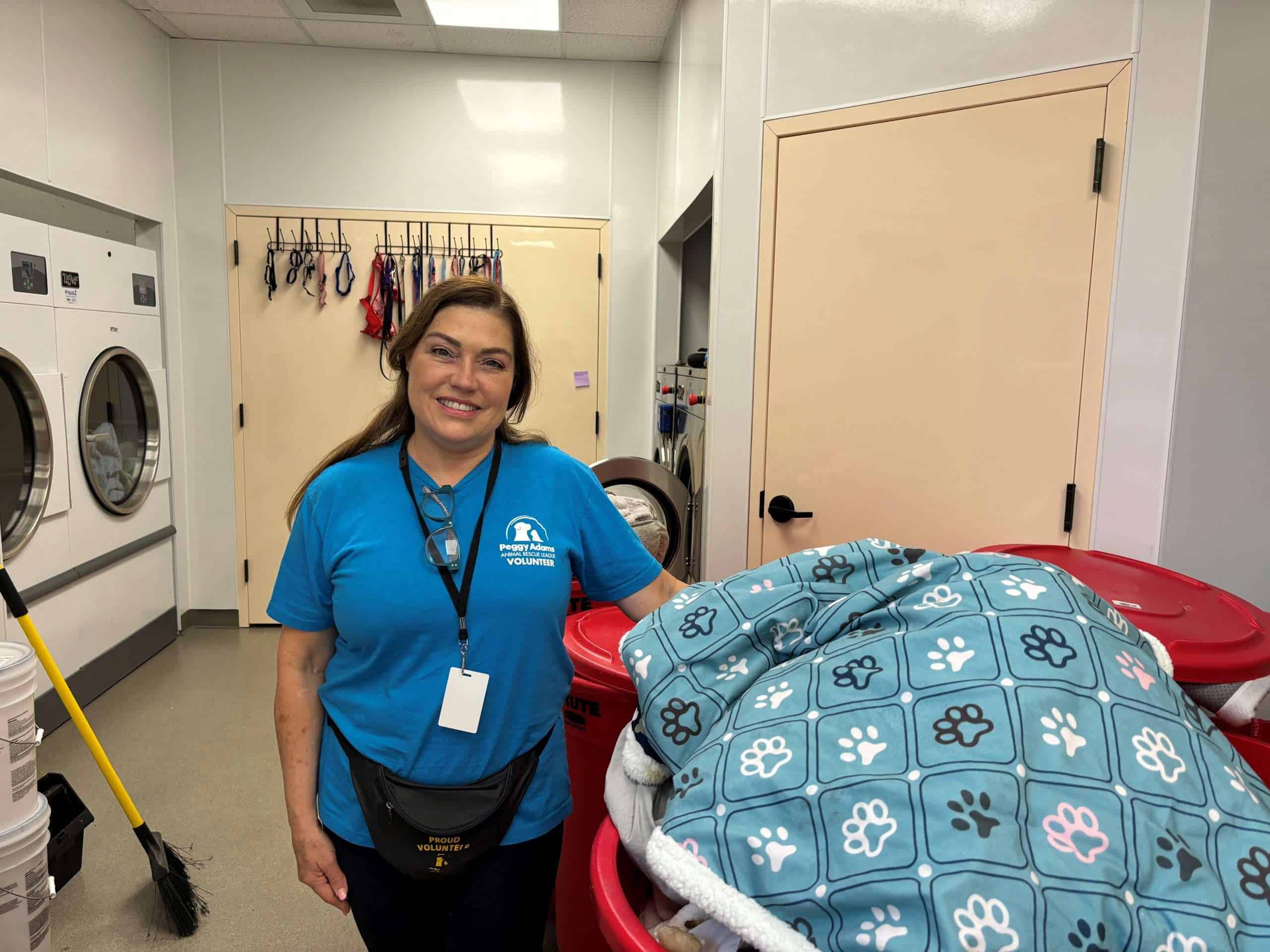 Volunteer smiling next to laundry area with pet bedding and supplies.