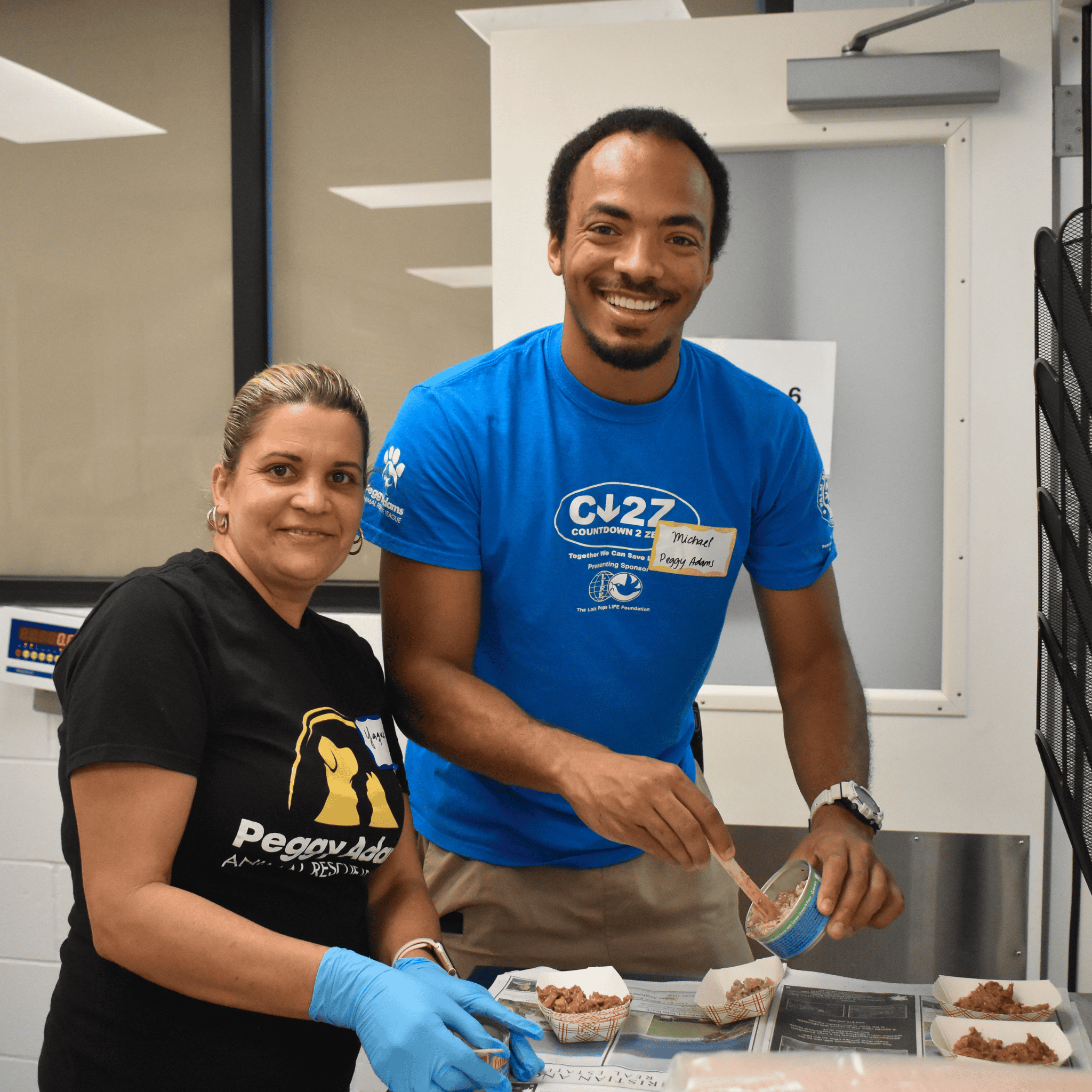 Two volunteers at Peggy Adams Animal Rescue preparing food for a dog adoption event.