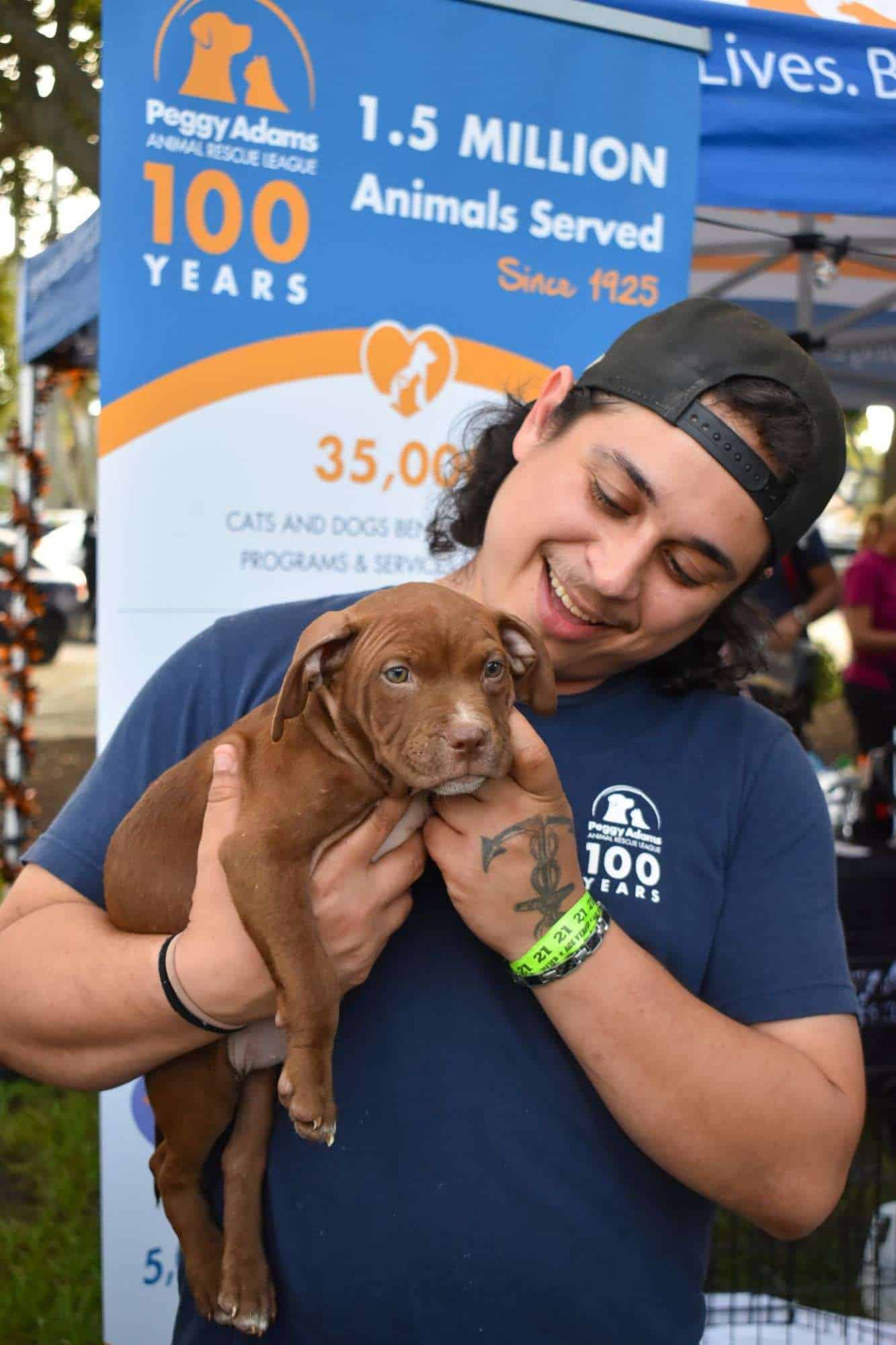 Woman holding a brown puppy at Peggy Adams animal rescue event.