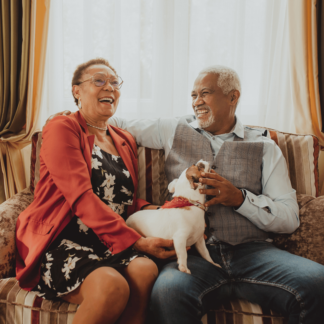 Happy senior couple with small dog on sofa in living room.